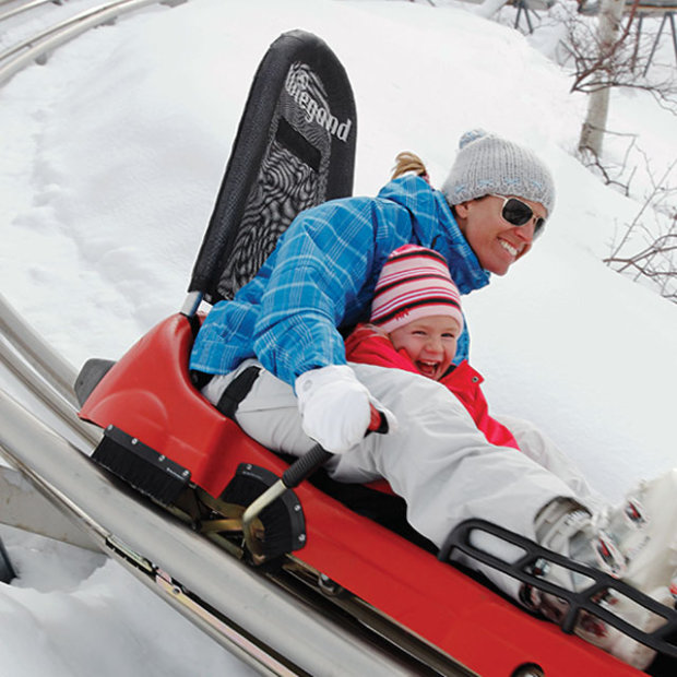 picture of a mom and child smiling as they ride the Alpine Coaster down a snow-covered mountain