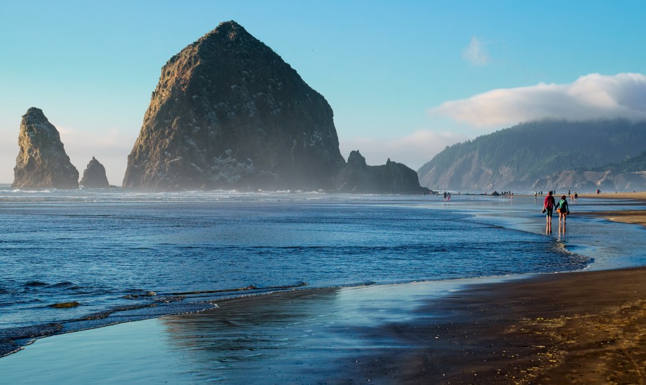 picture of Haystock Rock jutting from the beach with people walking by in Cannon Beach, Oregon