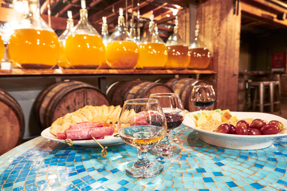 Superstition Meadery table set with wine glasses and appetizers in front of wine barrels and mead jugs.