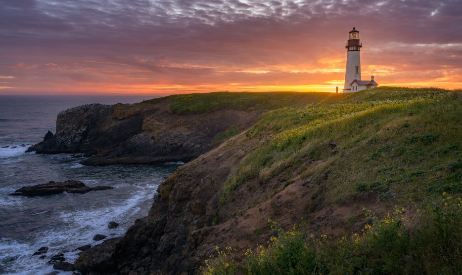 Yaquina Head Lighthouse in Newport, Oregon, at sunset with waves crashing