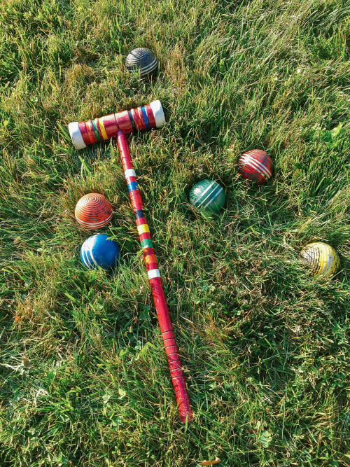 a red croquet mallet with a colorful croquet balls lying on grass