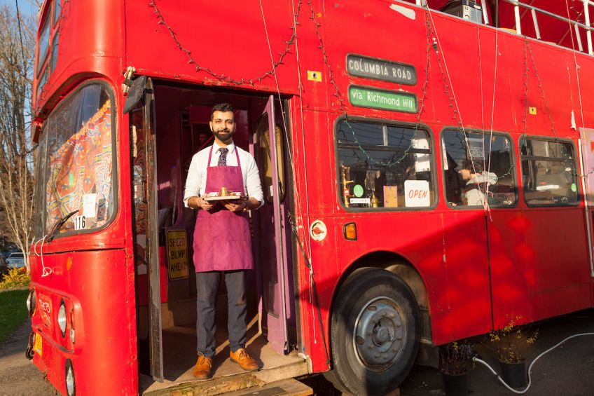 bearded barista in apron holds coffee tray and stands in the doorway of Tov coffeehouse, a converted double-decker bus, in Portland, Oregon, picture