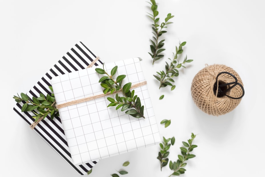 Two presents wrapped with graphic wrapping paper and natural twine are topped with a small twig or sprig of greenery, photo