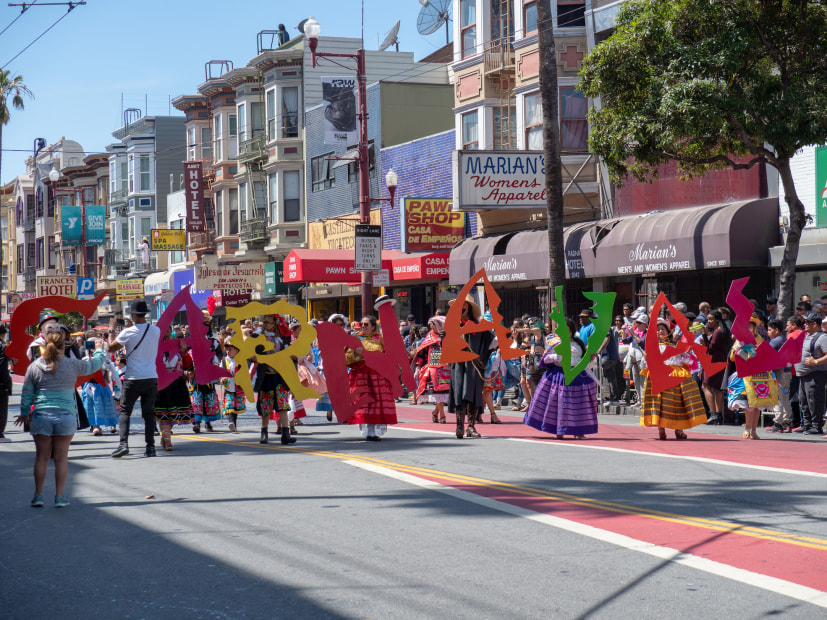 Picture of a colorful parade heading down Mission Street spelling out Carnaval