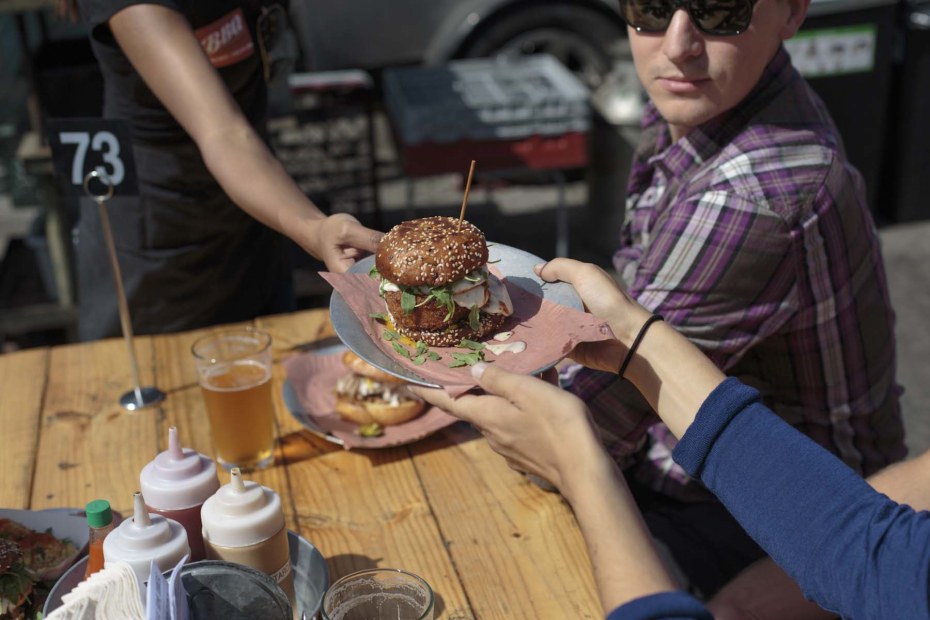 a diner takes a hefty sandwich at an outdoor table at 4505 Burgers & BBQ, San Francisco, picture