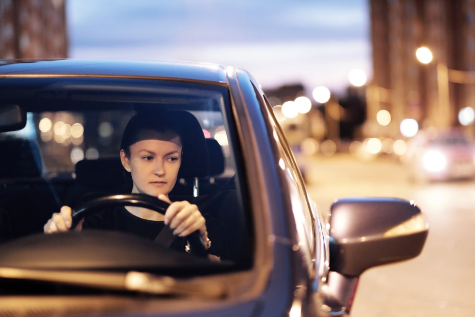 A woman driving at night is lit up by a streetlight.