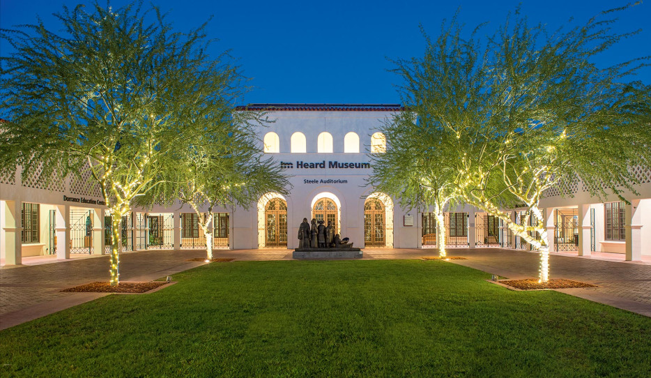 Heard Museum entrance across courtyard with figural sculpture and lawn lined by cottonwood trees with string lights, at twilight in Phoneix, Arizona, picture
