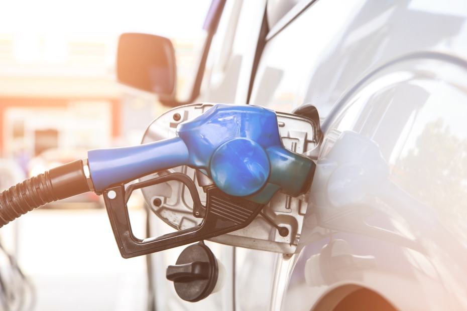 a blue fuel nozzle filling up gas tank on silver car at a gas station