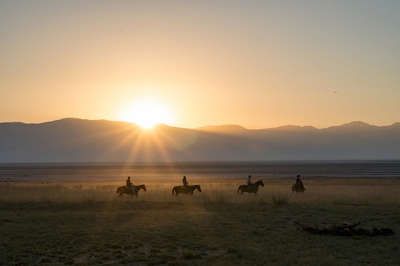 four riders on horseback tour follow a trail as sun peeks over mountains near Fielding Garr Ranch on Antelope Island in the Great Salt Lake, Utah, picture