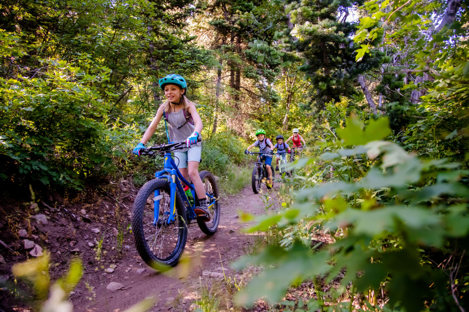 A girl leads her family down a downhill mountain biking trail at Snowbasin, image