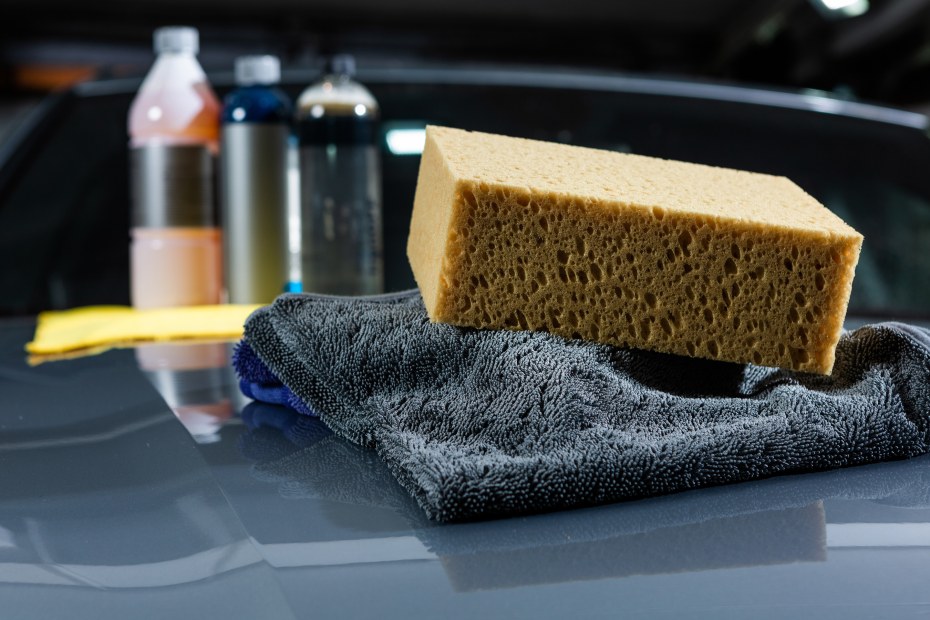 yellow sponge and gray cloth sitting on car with car wash soap in the background