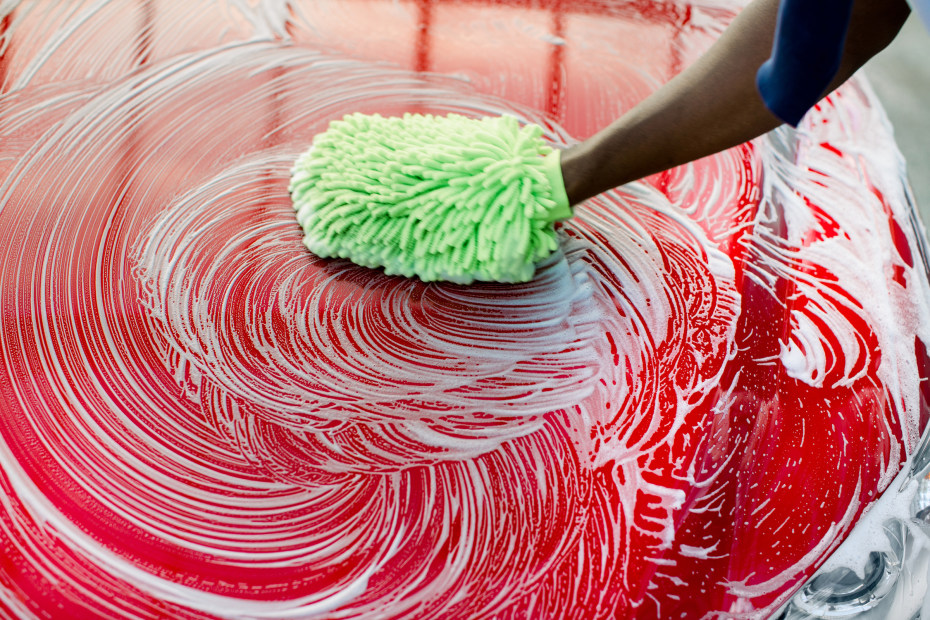 a hand uses a green mitt to wash the exterior of a red car