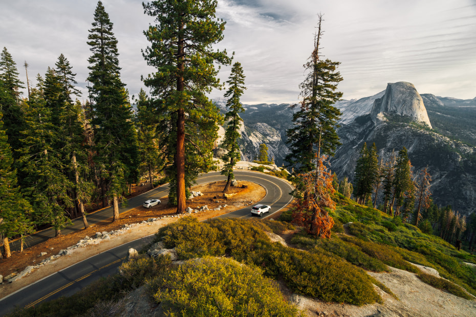 sharp turn on the road to Glacier Point in Yosemite with half dome illuminated by the sunset in the background.