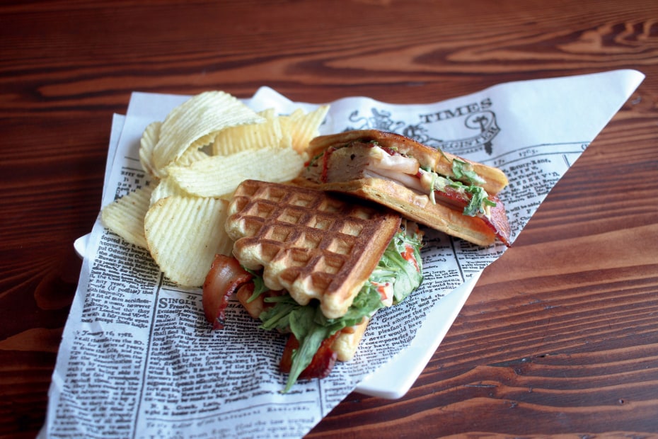 Waffle sandwich with ham, turkey, arugula, and served with ridged chips on newsprint at the Portland Press in Salem, Oregon