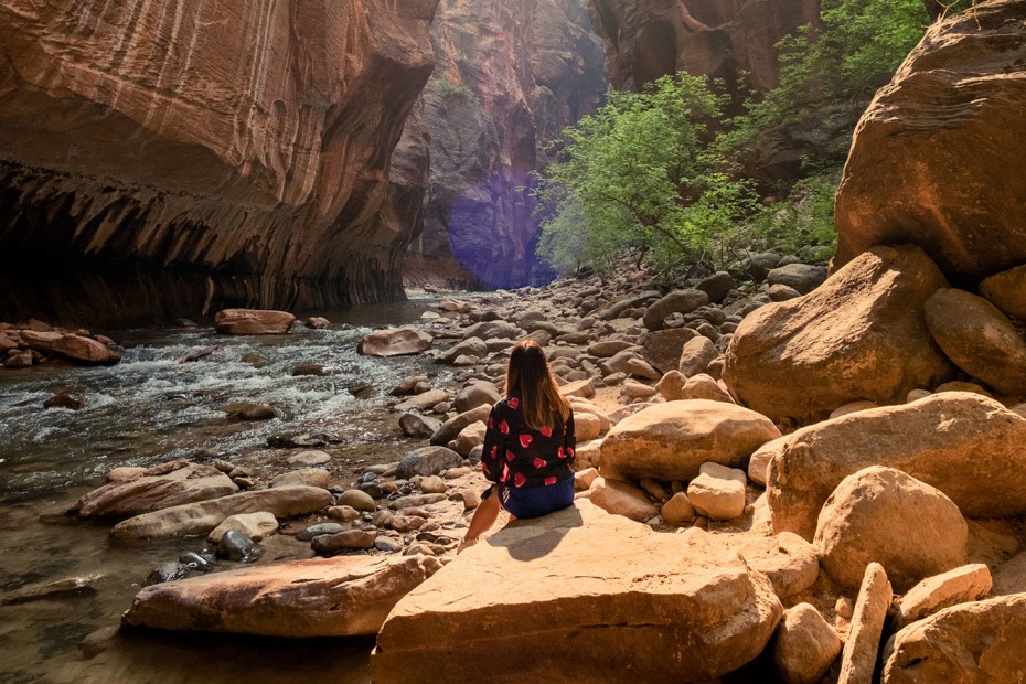 young woman sits on rock beside stream in The Narrows canyon at Zion National Park, picture
