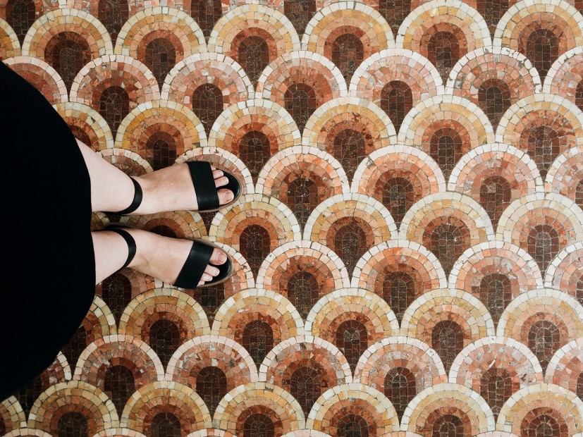 downward perspective of woman in black skirt with black open-toed shoes on mosaic of interleaved arch pattern floor tiles, picture