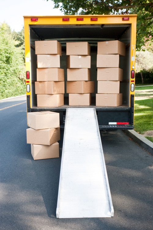 View of parked moving truck from behind packed with stacked boxes and loading ramp extended down, picture