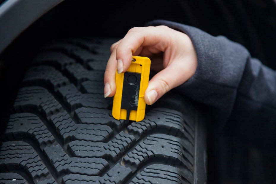 A woman inserts a tire depth gauge into the tire to check the tire tread depth, image