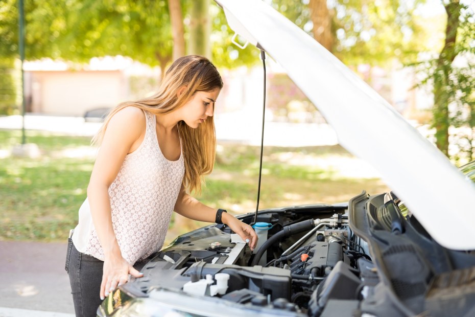 a woman looks under the hood of a car, image