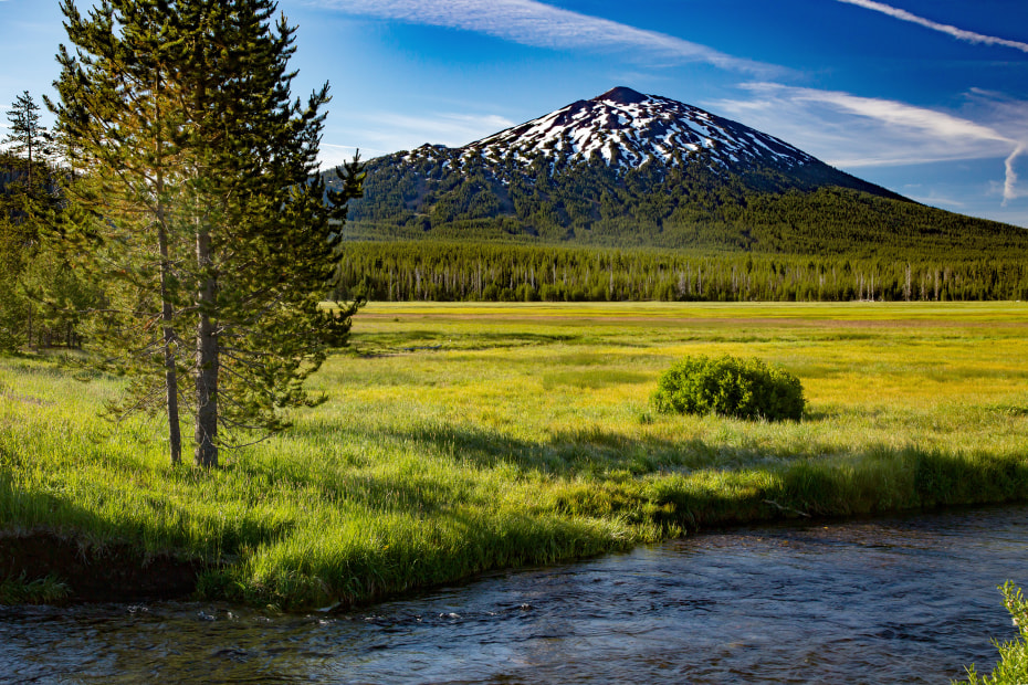photo of a green meadow on the edge of a blue lake with a snowy Mount Bachelor in the distance