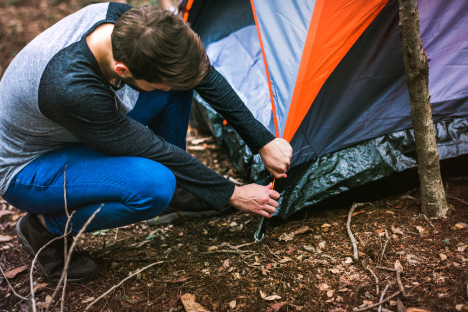 A man attaches a rainfly to the corner of his rented tent