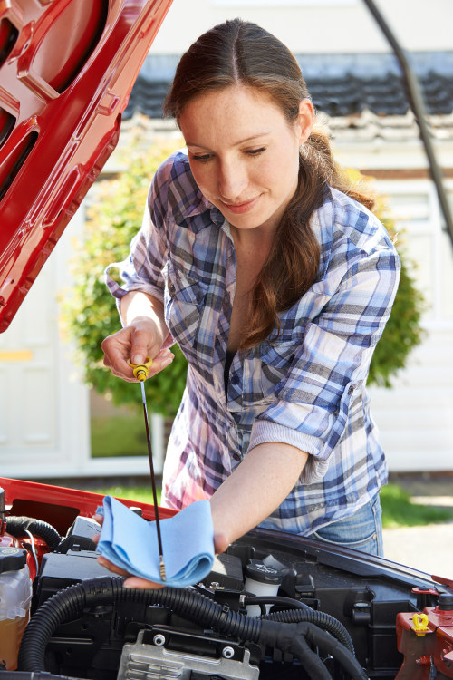 A woman wipes the engine oil dipstick clean.