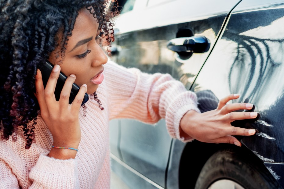 A driver inspects hit-and-run damage on her car.