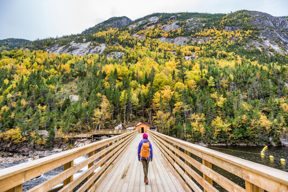 A woman walks on a footbridge in autumn with fall colors in the background, image