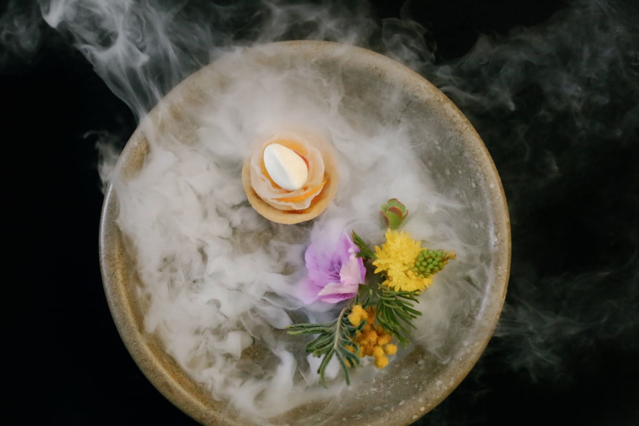 view from above of poetic plate offering with dry ice vapors and exotic floral-herb garnish at Atelier Crenn in San Francisco