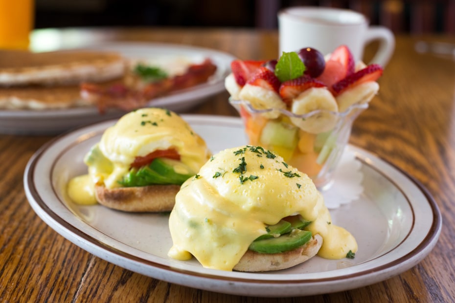 Photo of eggs benedict with avocado on a plate with fruit at Fire Sign Cafe