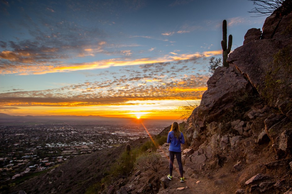 the sun rises over Phoenix, Arizona, as a woman watches while hiking