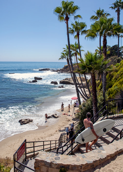 surfer with board climbing stairs looks back towards Picnic Beach and spectators in Laguna Beach