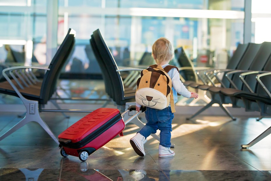 A toddler pulls a red suitcase through the airport.