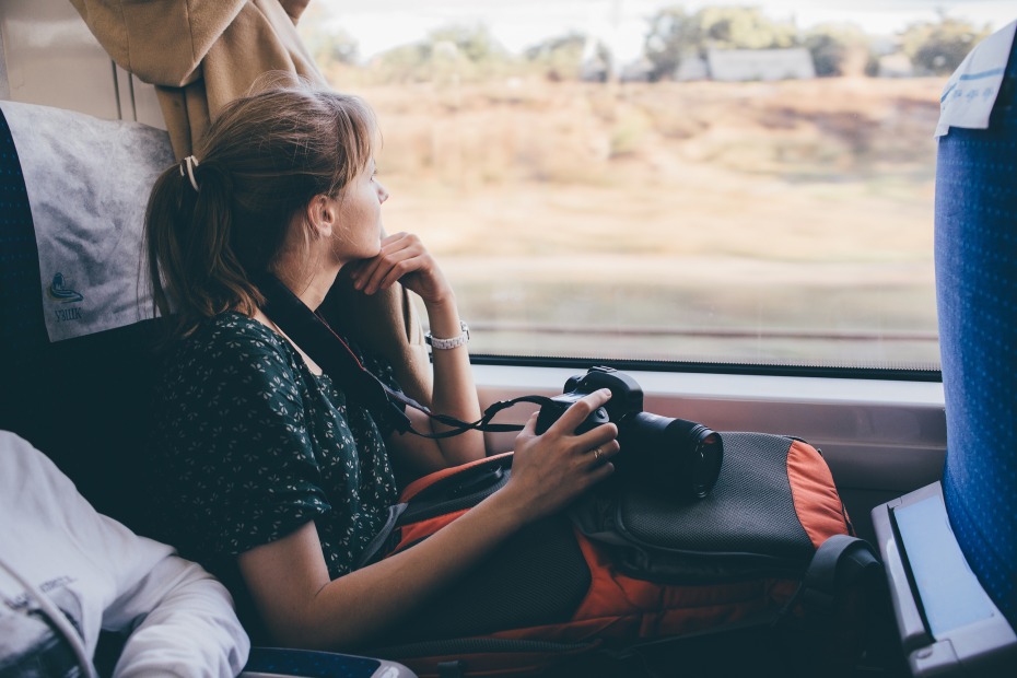 Female traveler looks out a train window with her camera.