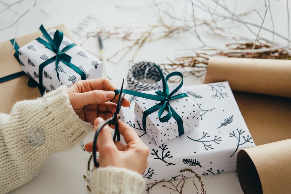 A person ties a green ribbon around a white holiday gift box.