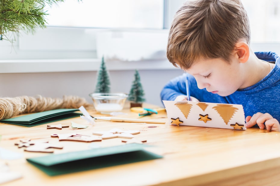 A child writes inside a handmade holiday card.