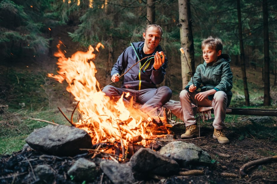 Father and son make s'mores over a campfire.