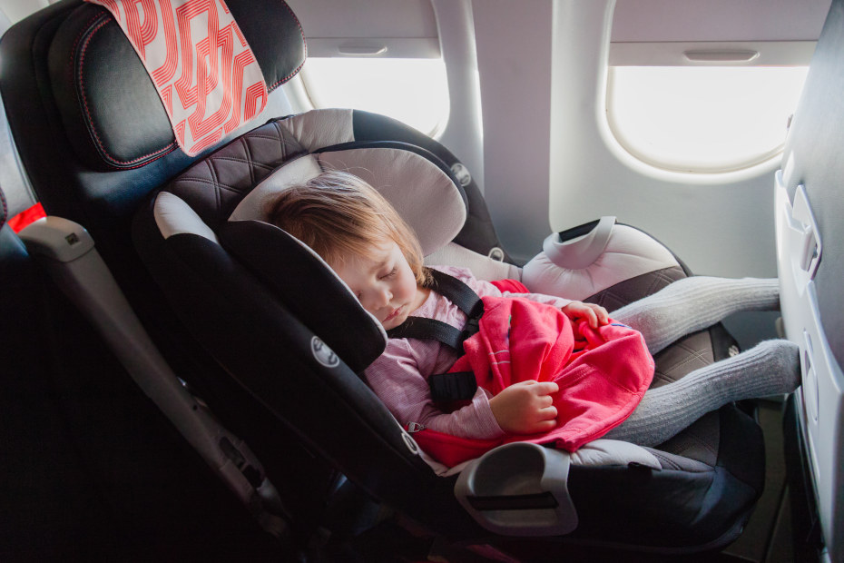 A girl sleeps in her car seat on an airplane.