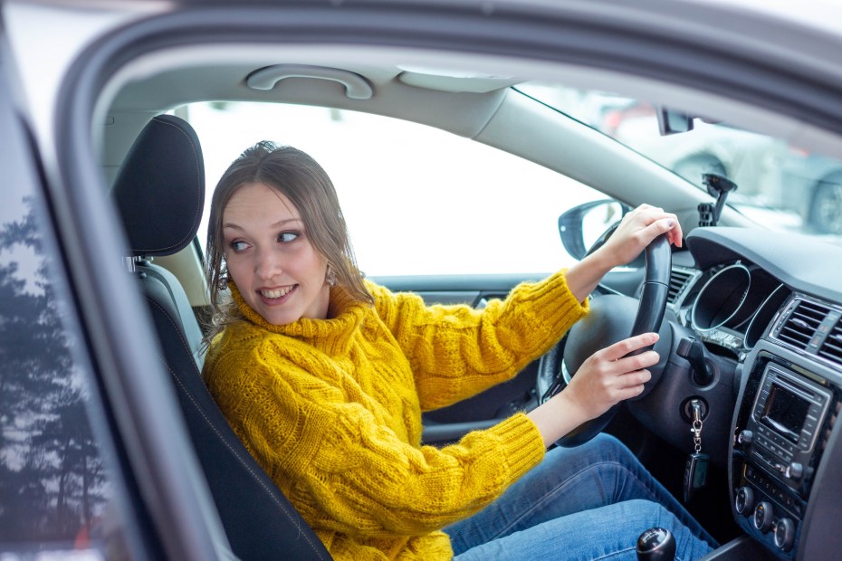 woman in a yellow sweater looking over her shoulder as she parallel parks her car