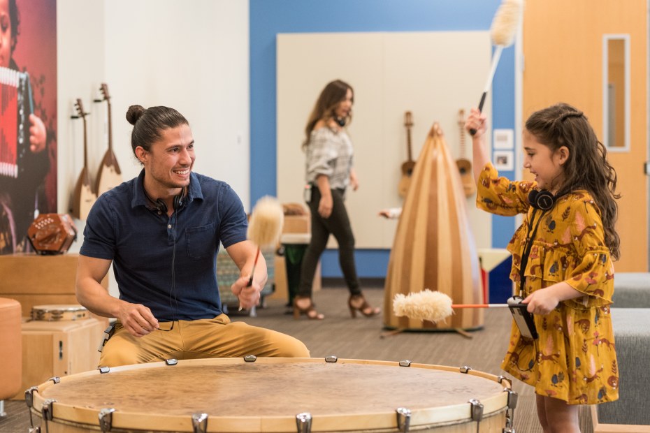 A girl plays a large drum with an adult at the Musical Instrument Museum in Phoenix, Arizona.