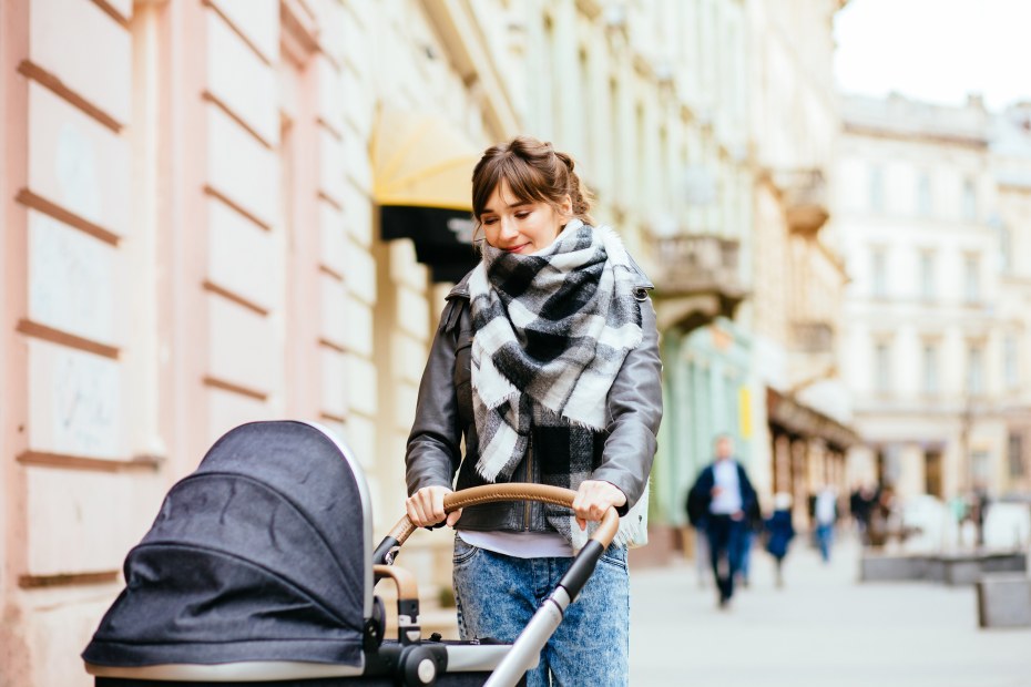 Mom walks European street with baby in a stroller.