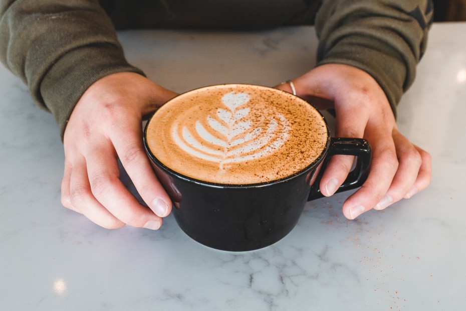 Hands hold a seasonal latte at the counter in Captain and Stoker.