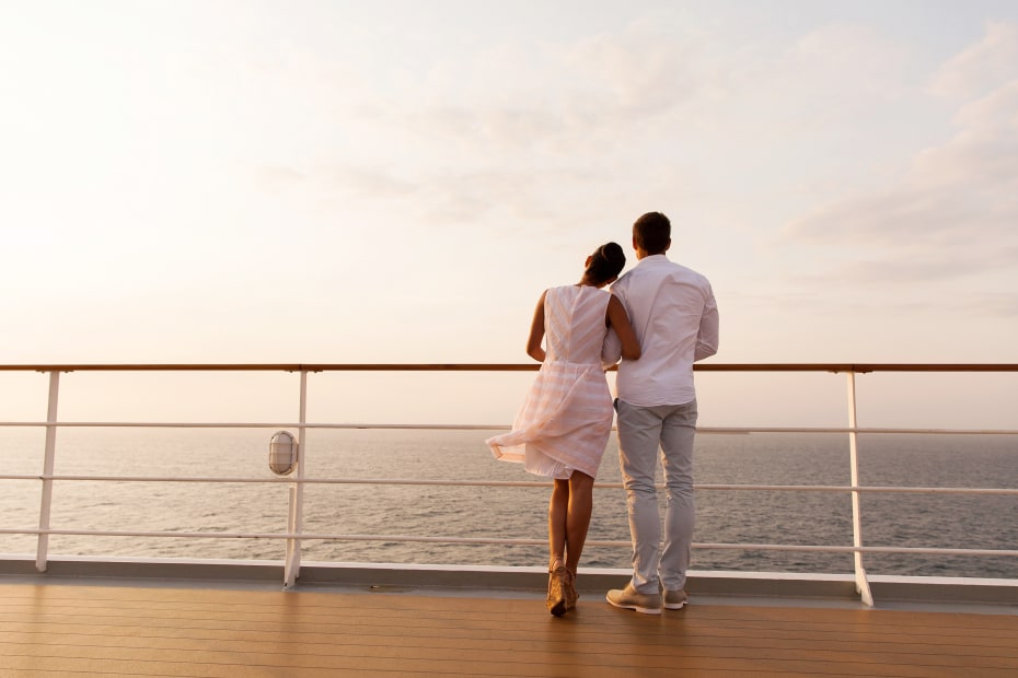 Man and woman stand on the deck of a cruise boat at sunset.