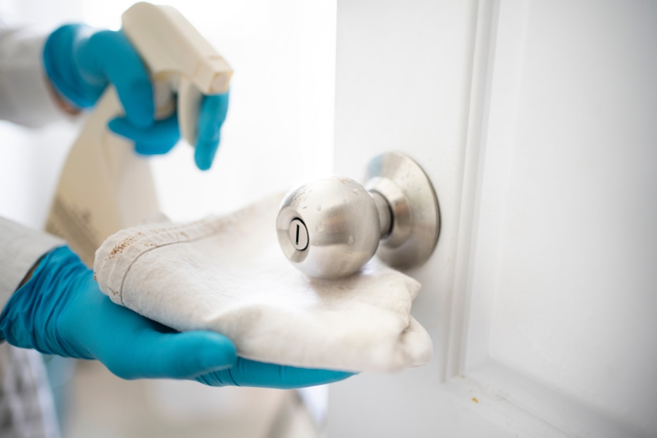 gloved hands spray cleaning fluid on a doorknob