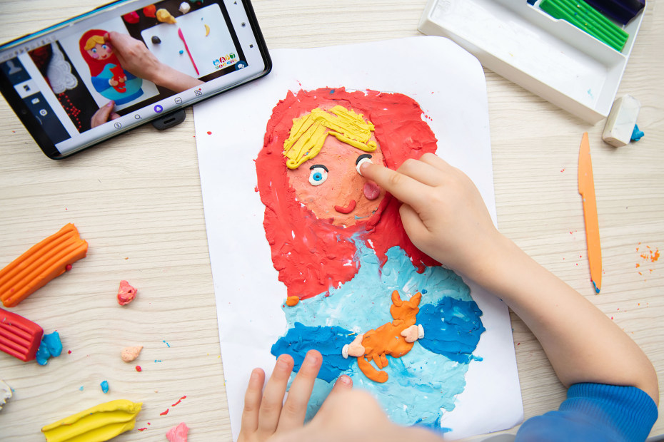 A child follows along to an art video on a tablet.