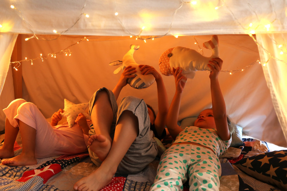 Three siblings playing in a fort under the dining room table.