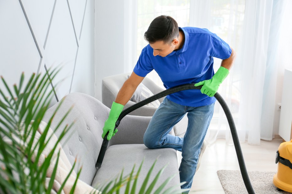 man in a blue shirt uses a vacuum arm to vacuum in a couch