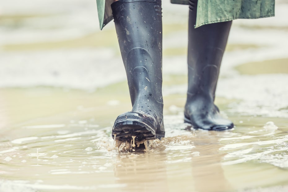 A person wears rubber rain boots to walk through muddy water.