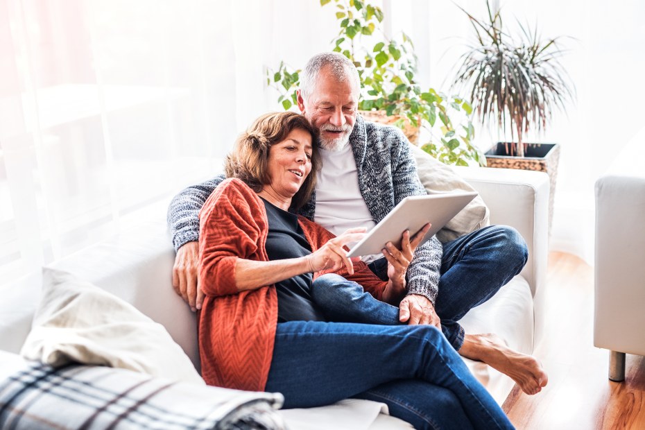 Senior couple look at a tablet together on the sofa.