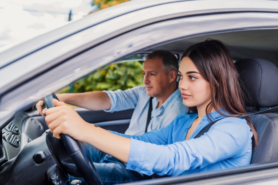 a young woman behind the wheel with a professional driving instructor in the passenger seat.